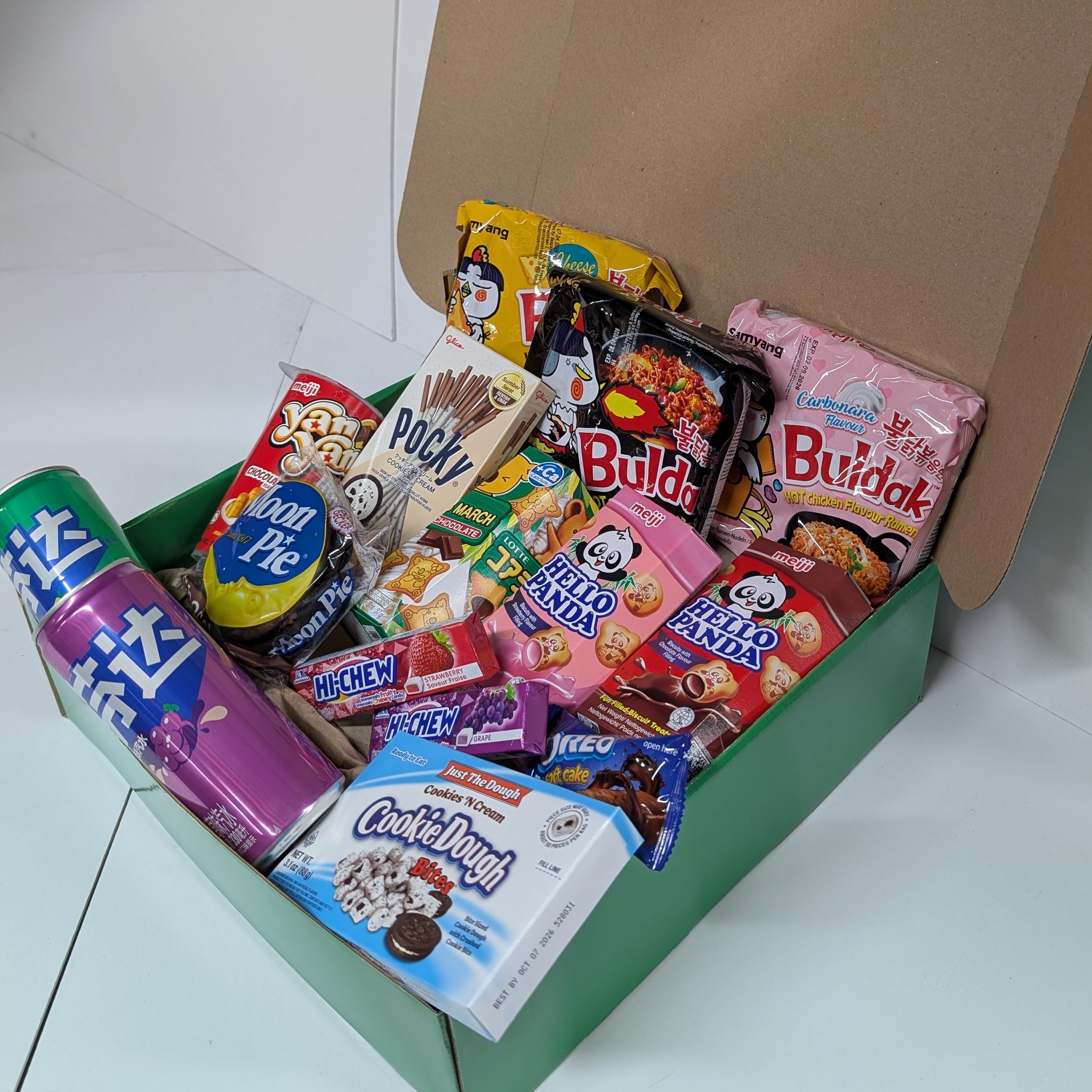 Assorted Japanese snacks in a green box on a white floor.