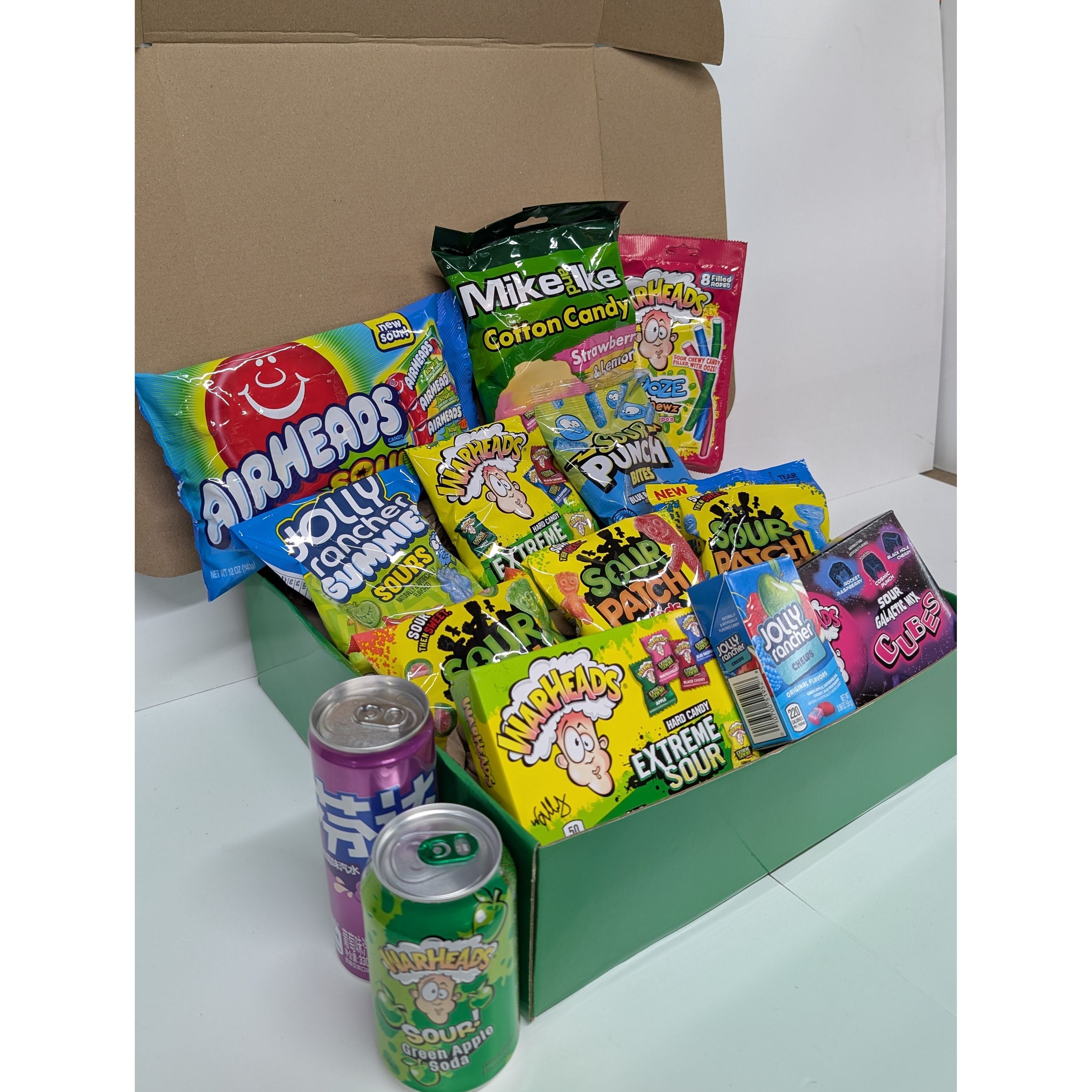 Assorted candy and soda cans in a cardboard box on a white background