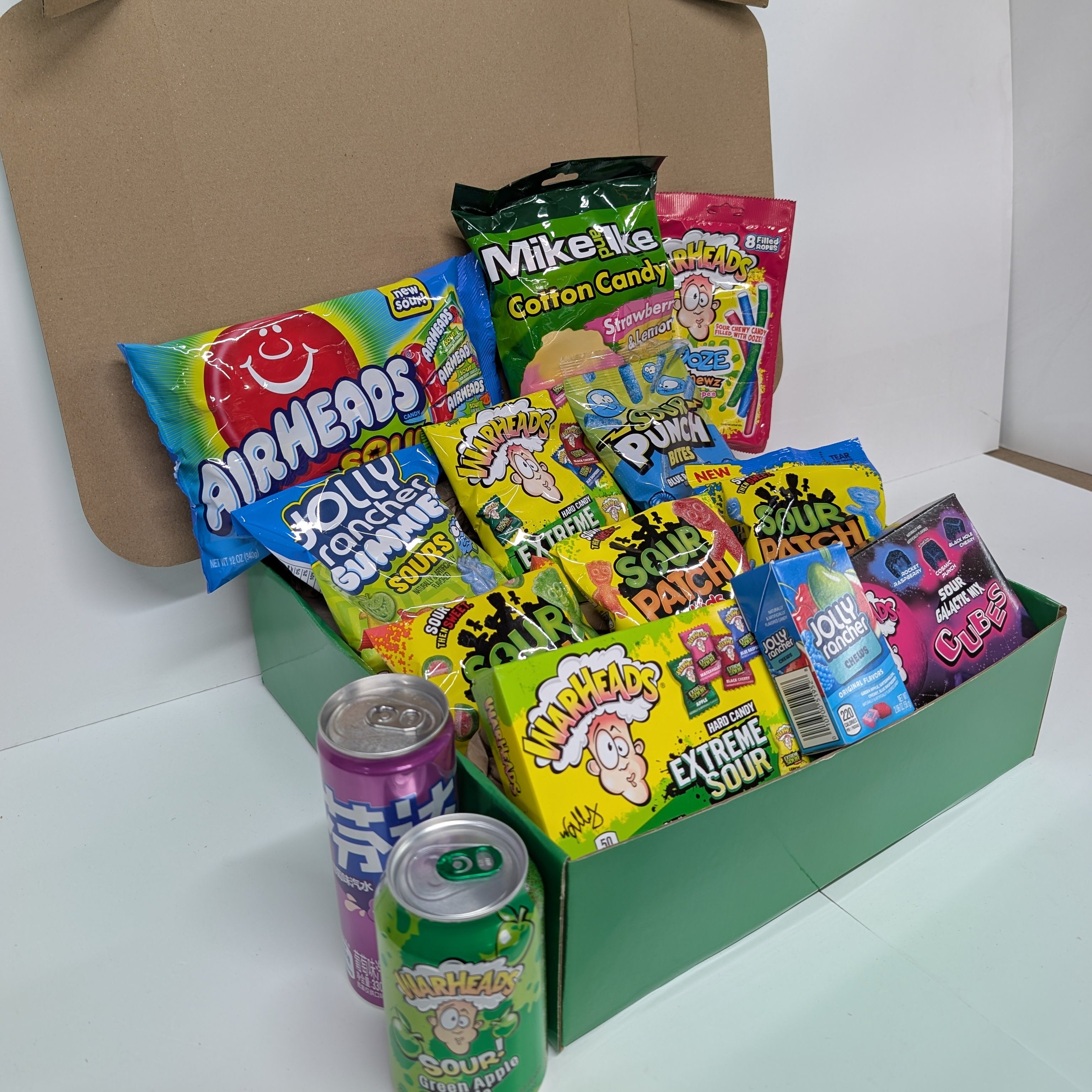 Assorted candy and soda cans in a cardboard box on a white background