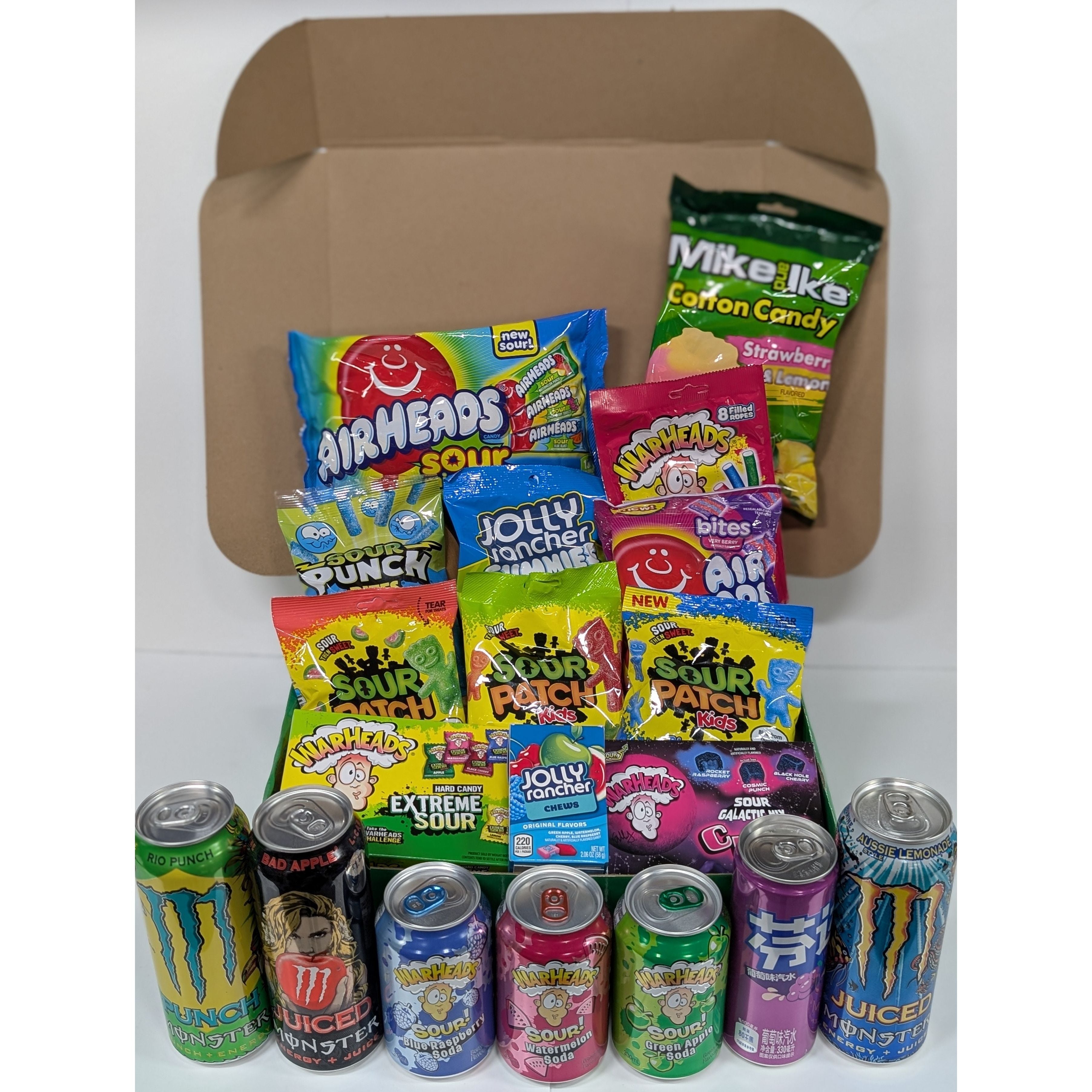 Assorted candy and energy drink cans in front of a cardboard box on a white background