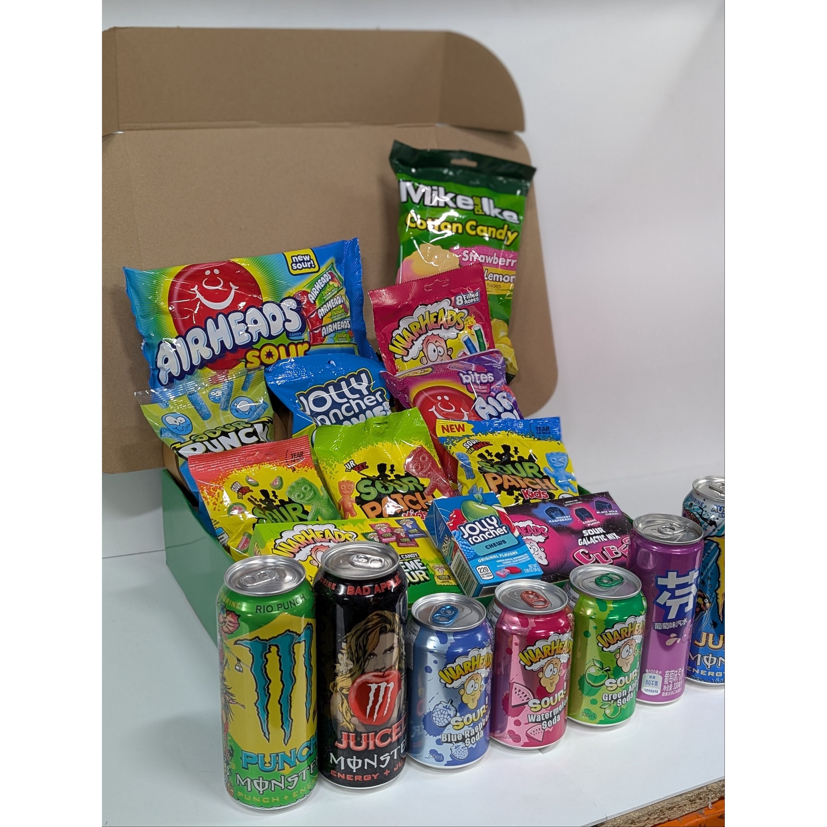 Assorted candy and energy drink cans in a box on a white surface
