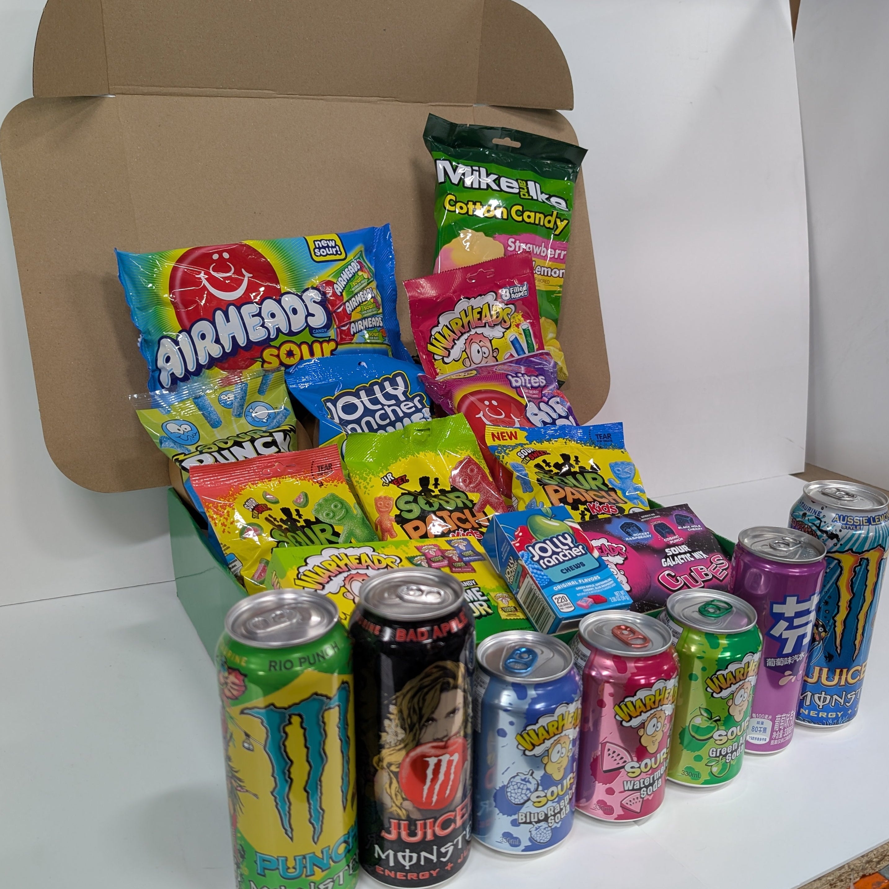 Assorted candy and soda cans on a white background with a cardboard box.